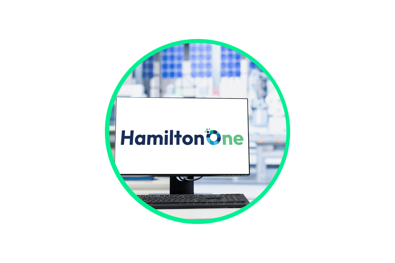Computer monitor displaying the HamiltonOne logo in a laboratory setting with shelving in the background