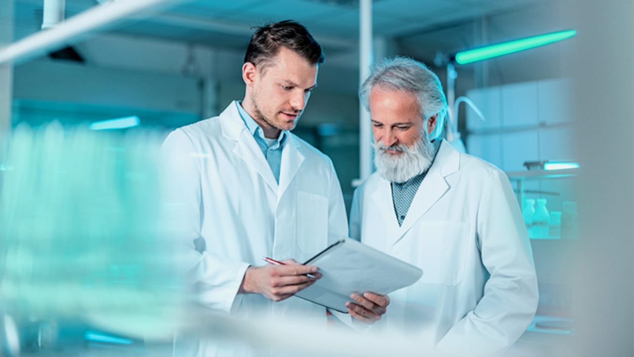 Two lab professionals in white coats reviewing documents in a laboratory setting.