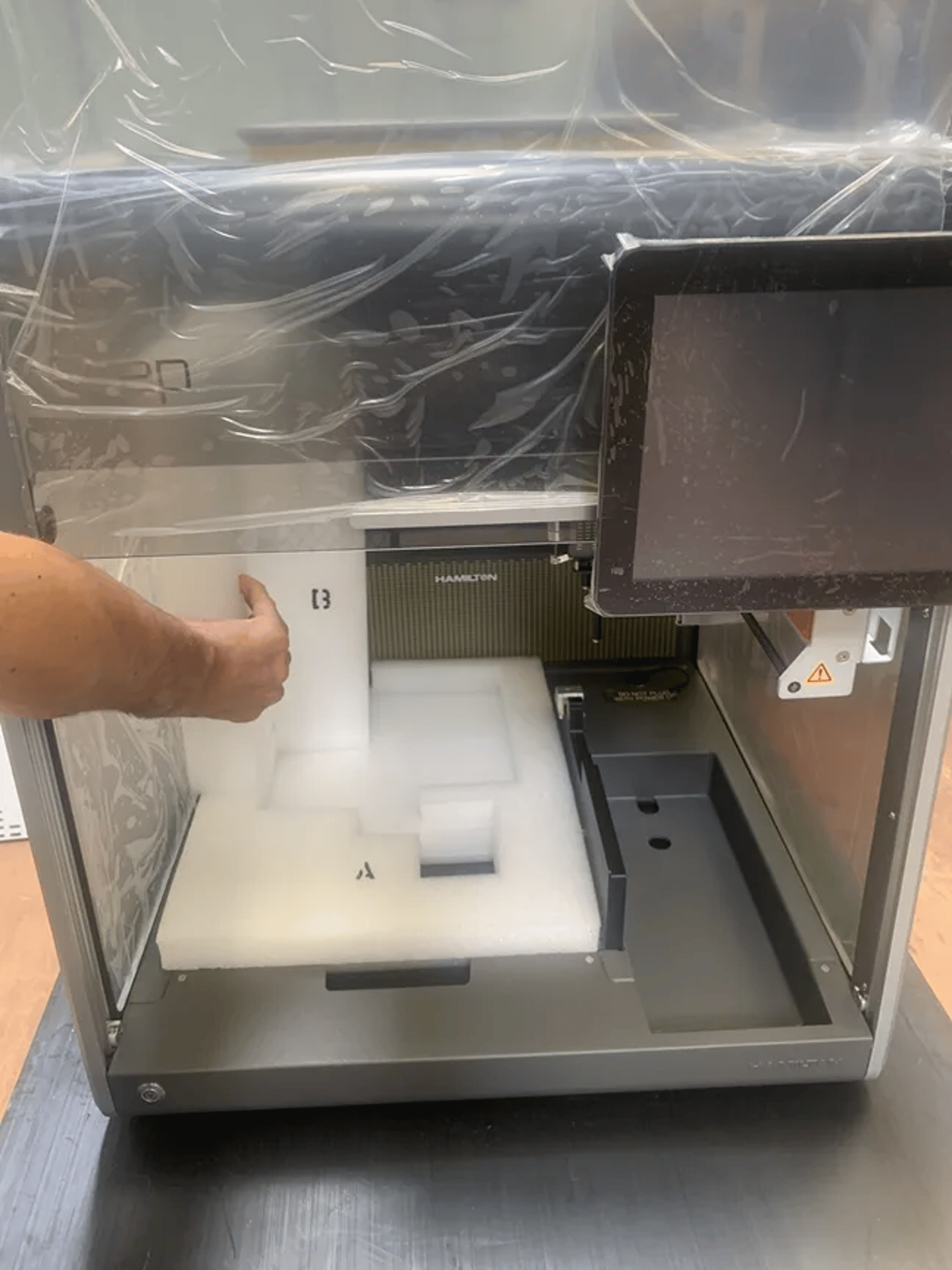 Hamilton automated liquid handler being unpacked, with foam packaging inside the enclosure and a touchscreen display