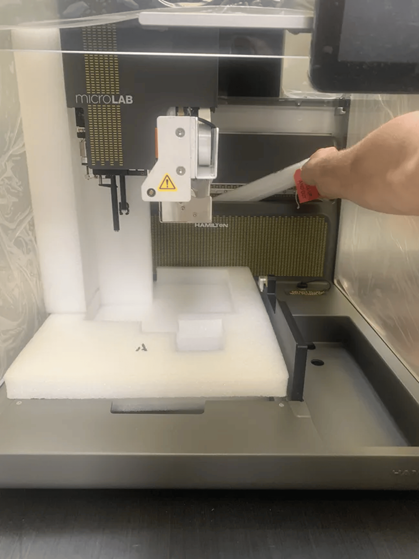 Hamilton MicroLab automated liquid handler with a person's hand inserting a tube into the instrument deck