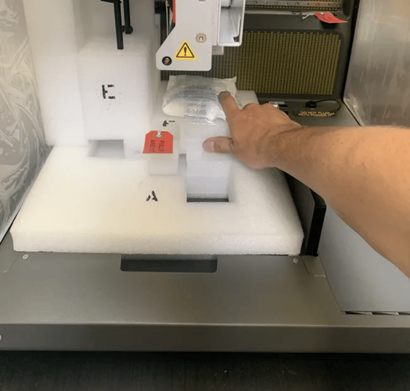 Hand pointing at foam-packaged component being inserted into a laboratory instrument