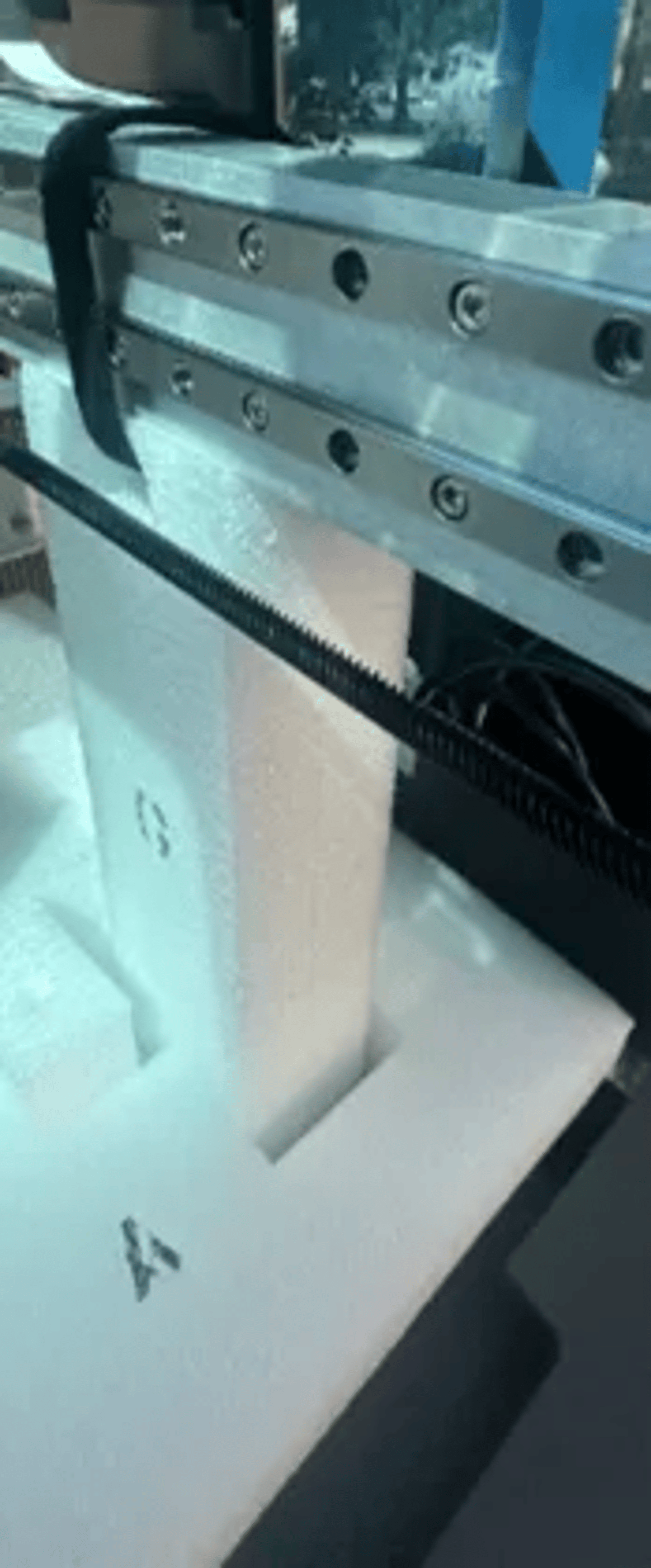 Close-up of a linear rail guide with rack and pinion mechanism on a white aluminum frame assembly