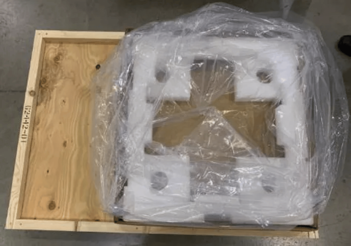 Foam-padded component wrapped in plastic inside an open wooden shipping crate