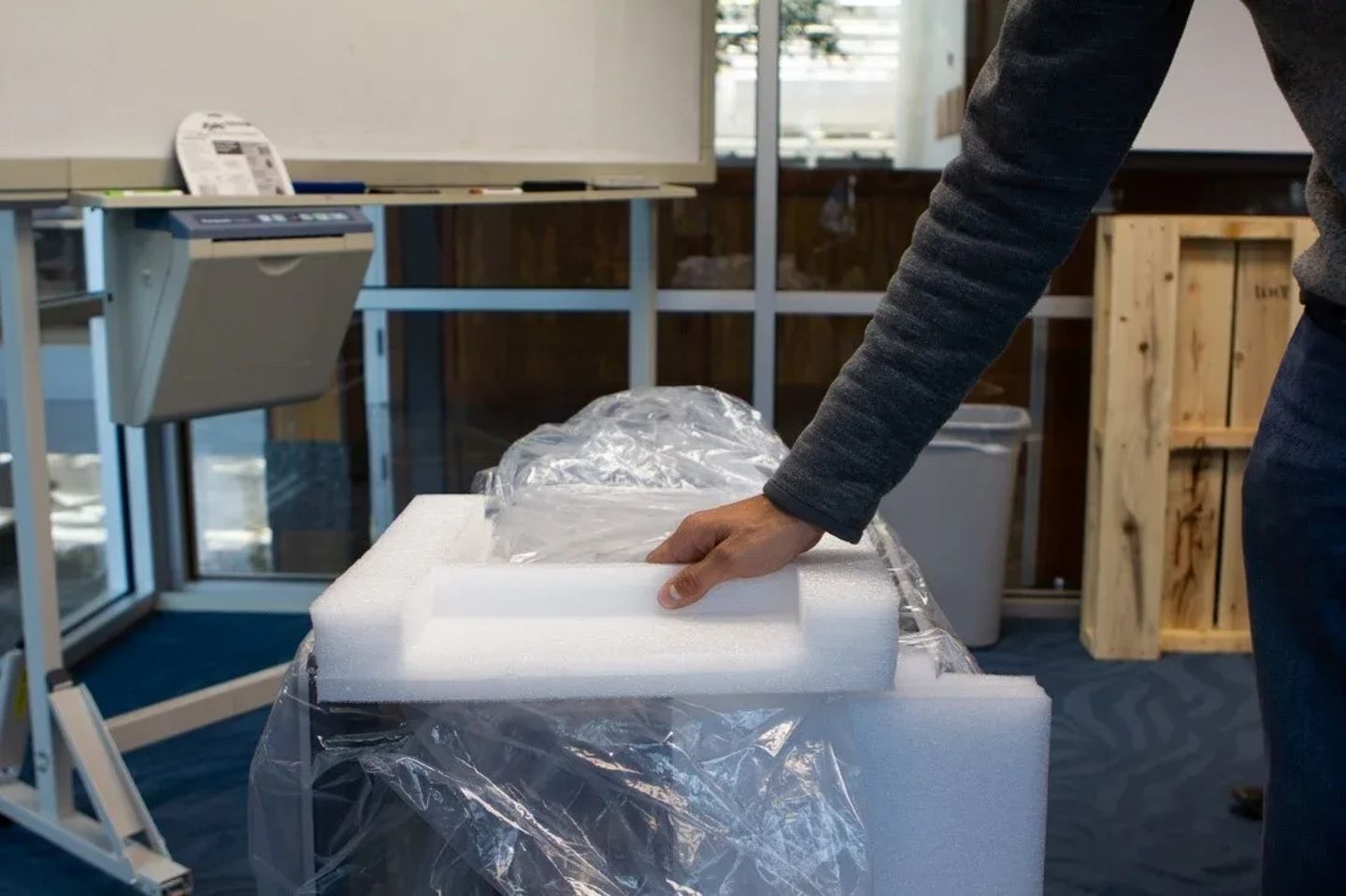 Person unpacking a laboratory instrument cushioned in foam padding and plastic wrap