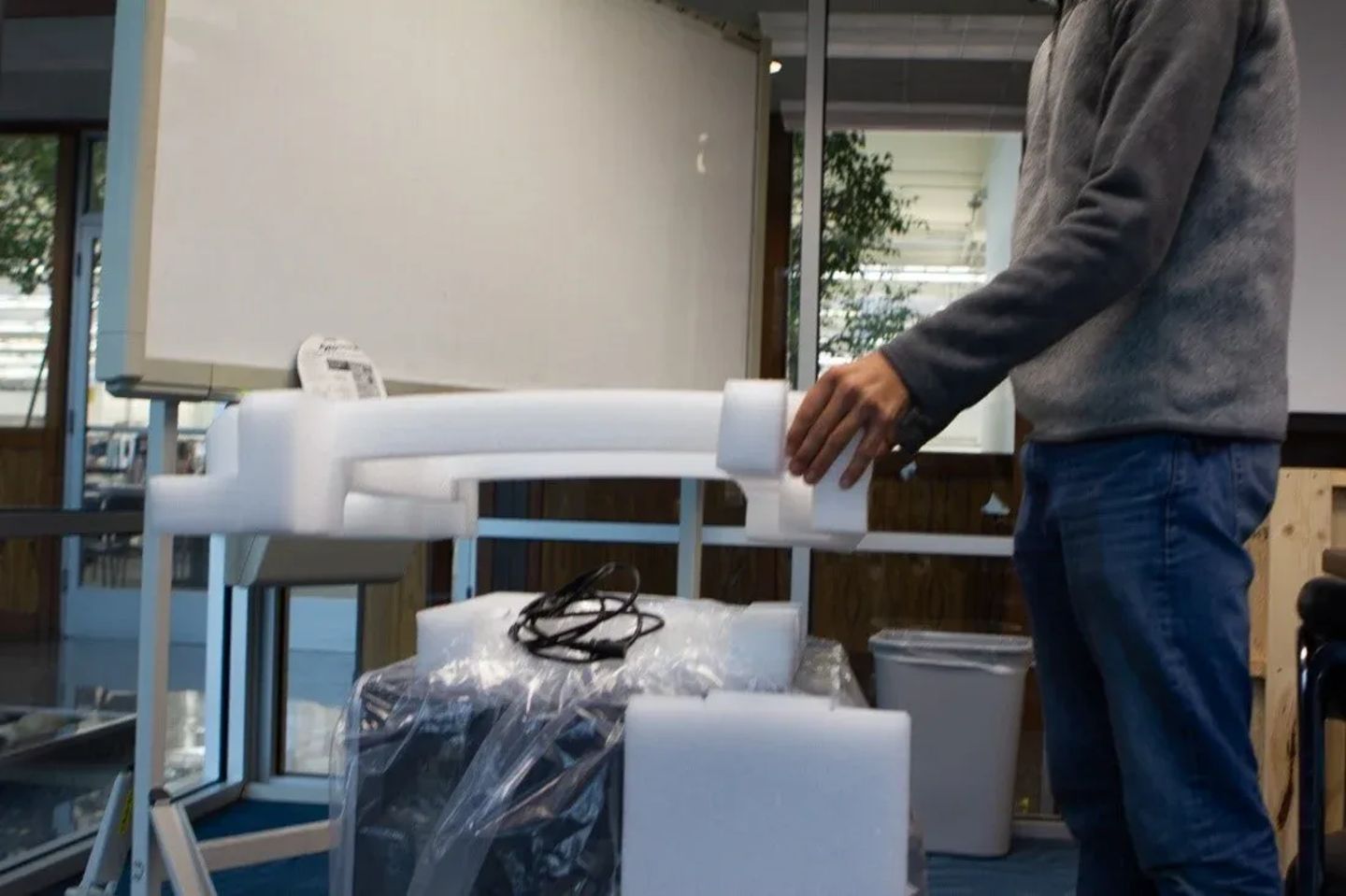 Person assembling a white laboratory instrument arm with foam packaging on a cart