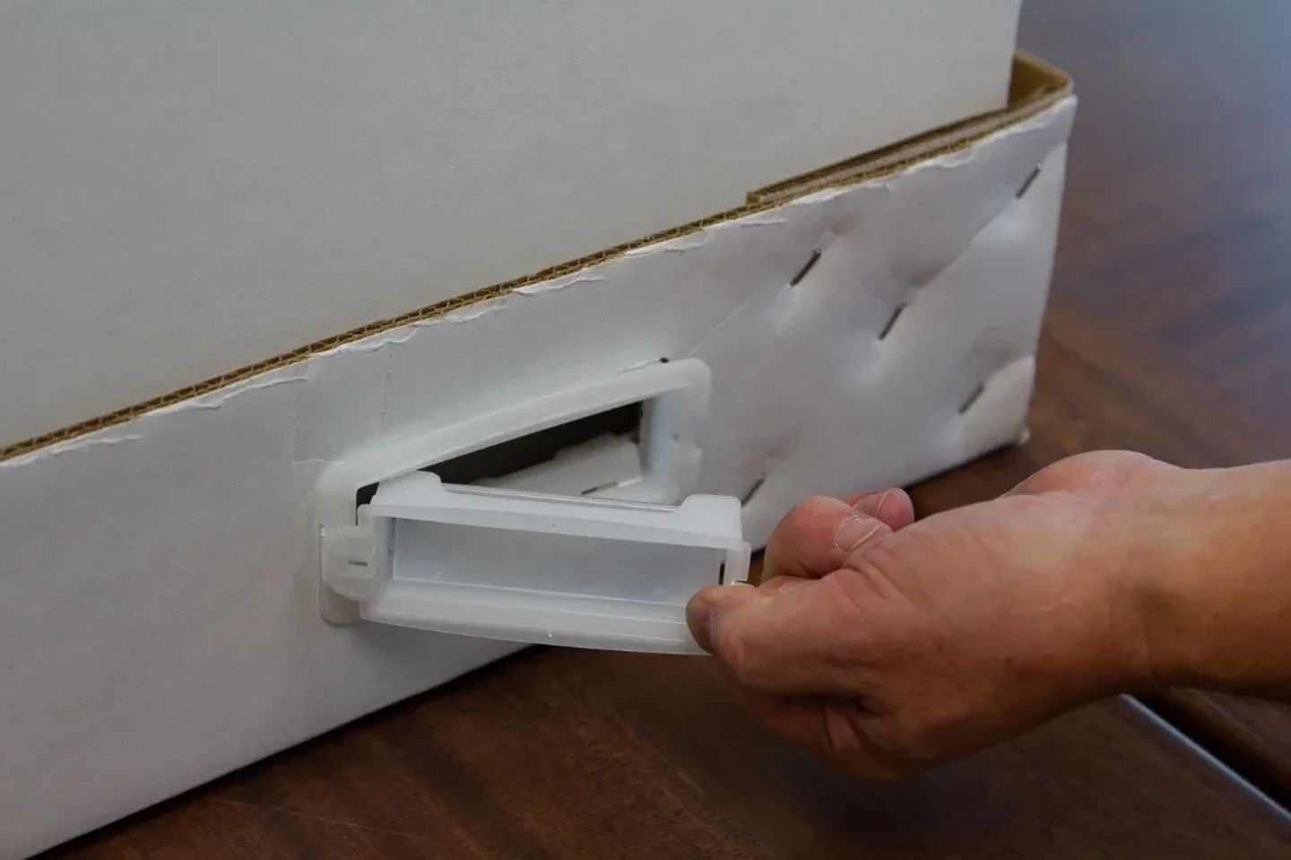 Hand removing a white plastic drawer or tray component from a cardboard-packaged instrument