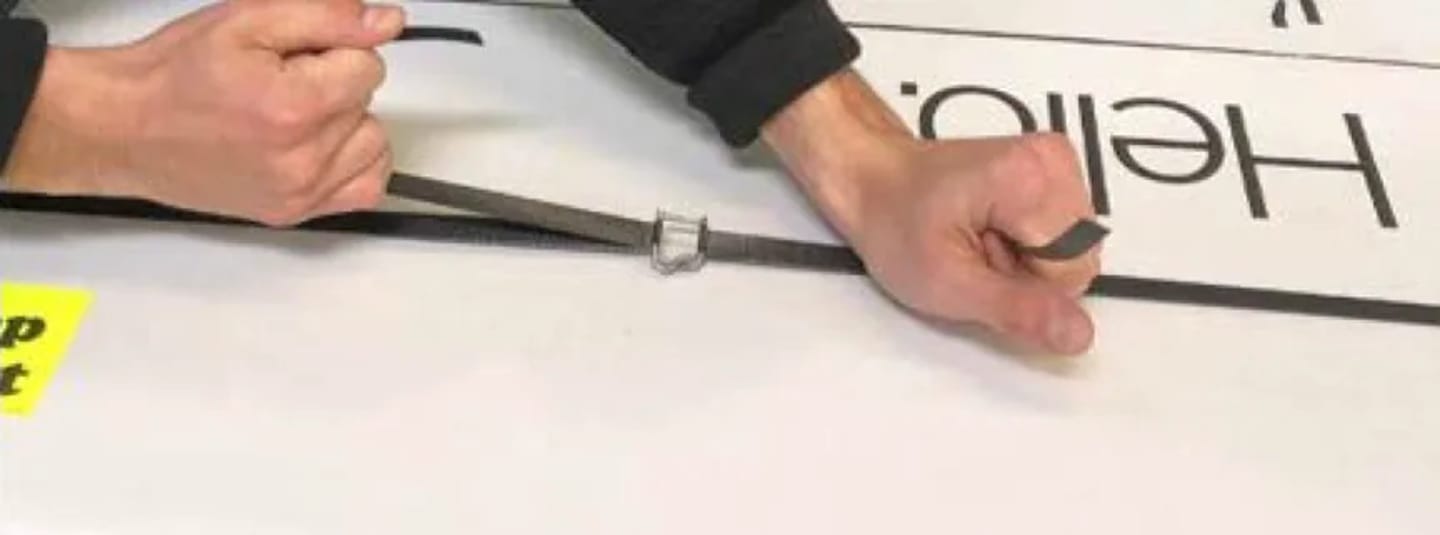 Hands adjusting a metal buckle on a gray strap against a white surface with mirrored "Hello" text