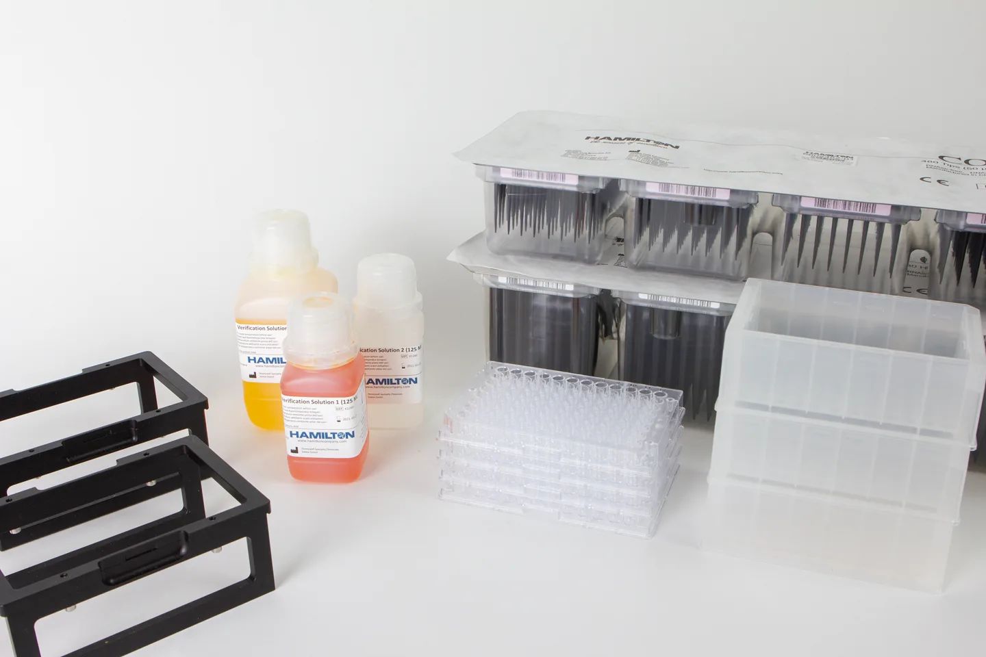 Hamilton verification kit components: colored verification solutions, pipette tip racks, microplate strips, and black plate holders on white surface