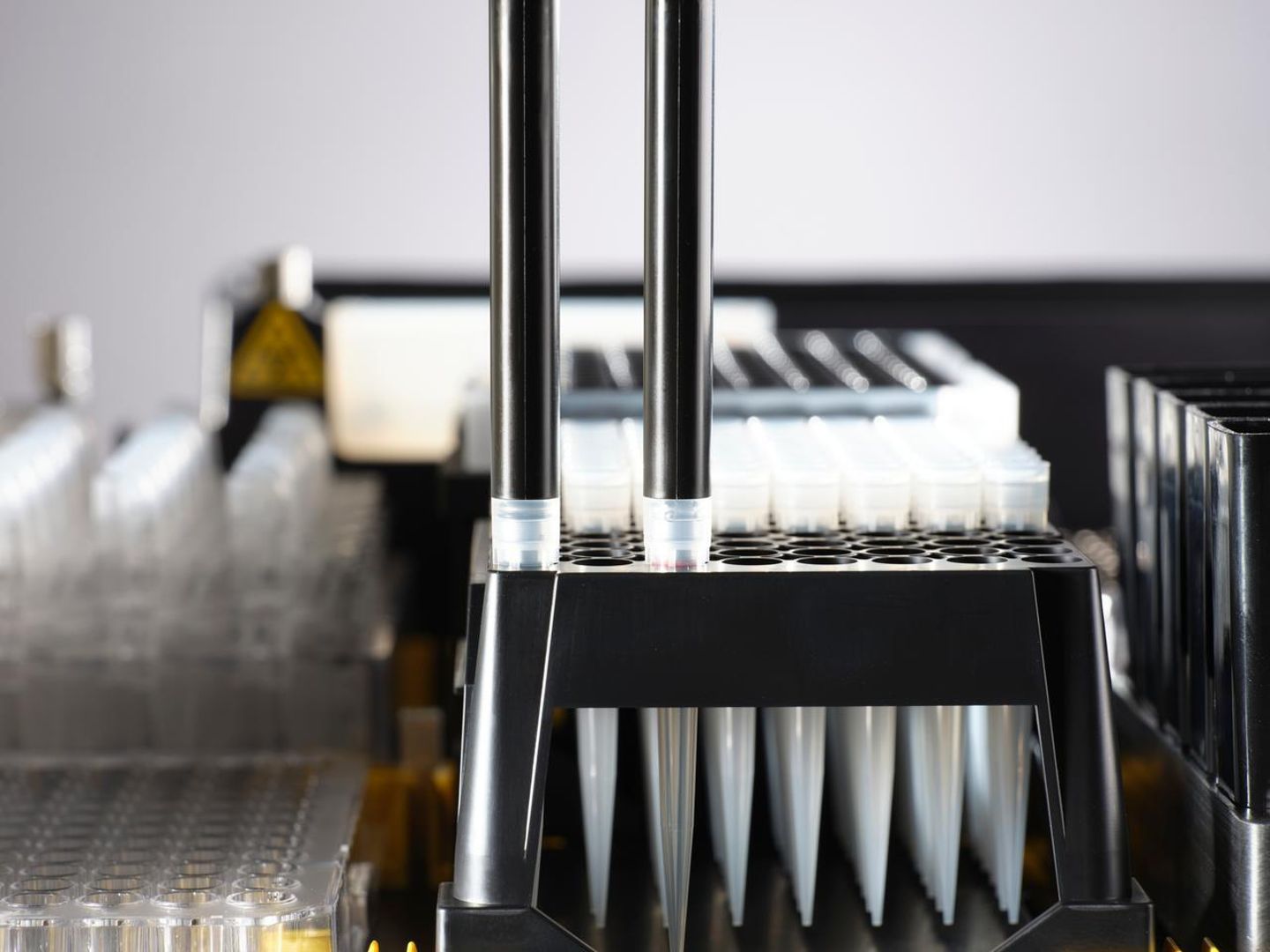 Automated liquid handler pipette arms picking up tips from a black tip rack