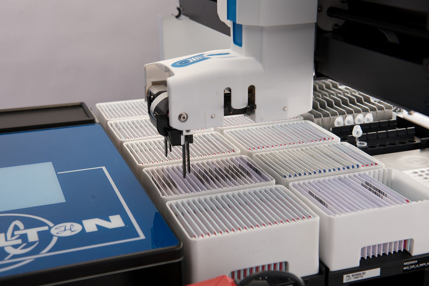Hamilton robotic gripper handling microscope slides arranged in white rack holders on a laboratory workstation