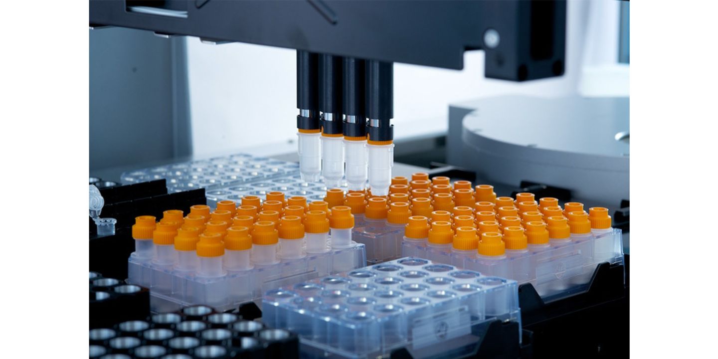 Automated liquid handler pipetting heads above sample vials with orange caps in plastic racks