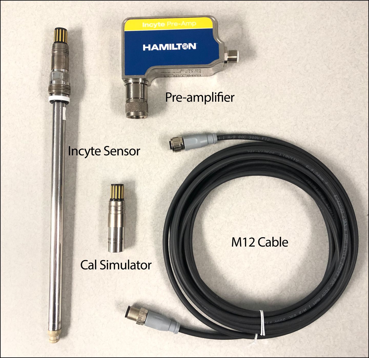 Hamilton Incyte sensor, Incyte Pre-Amp pre-amplifier, cal simulator, and M12 cable laid flat on a light surface.
