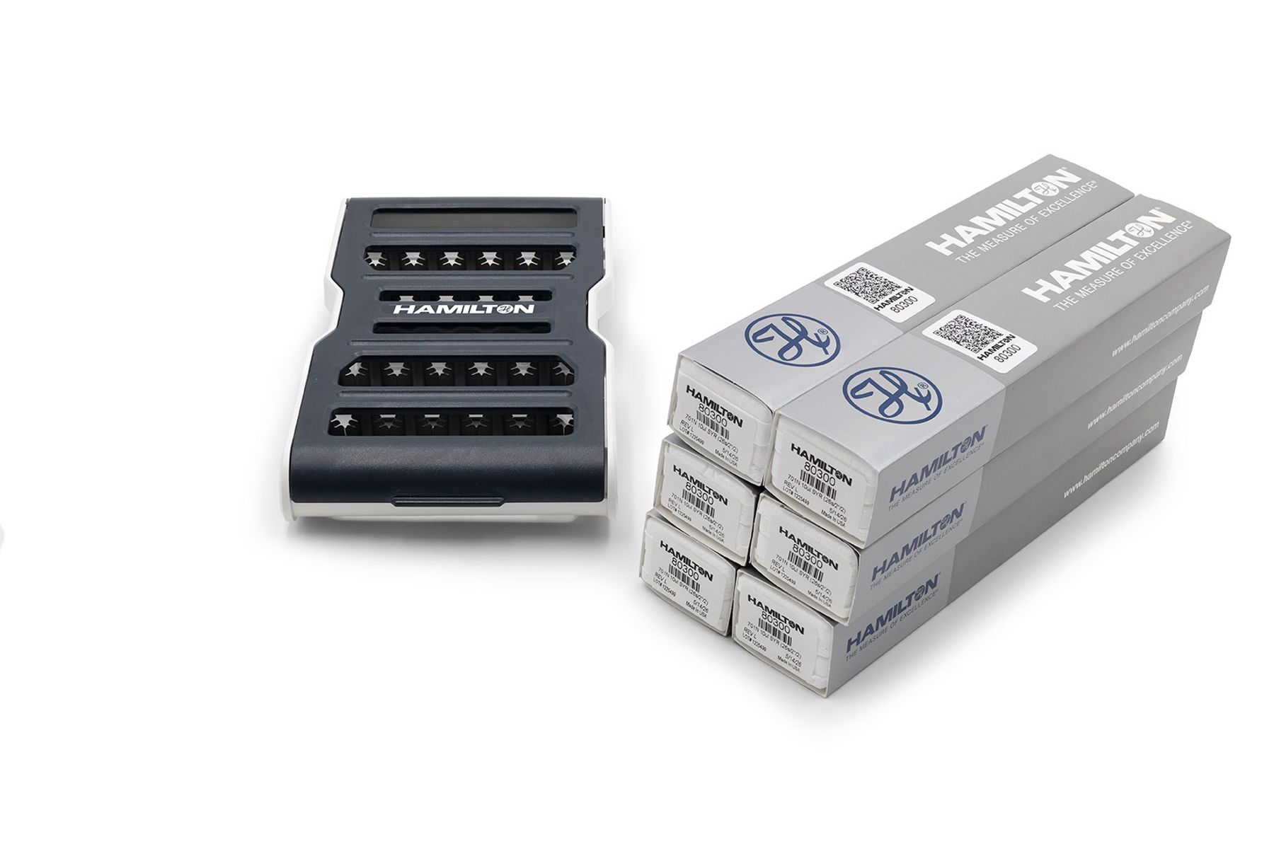 Hamilton syringe guard device beside six stacked Hamilton-branded product boxes labeled 80300