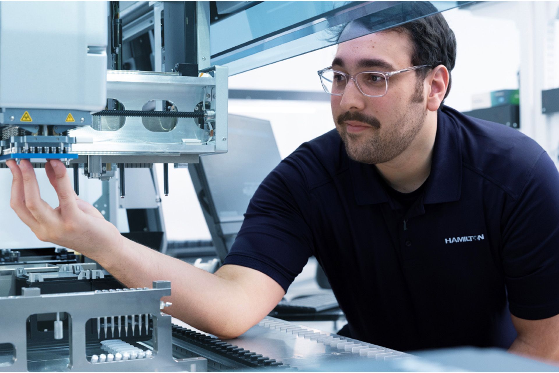 Hamilton technician in safety glasses inspecting pipetting needles on an automated liquid handler