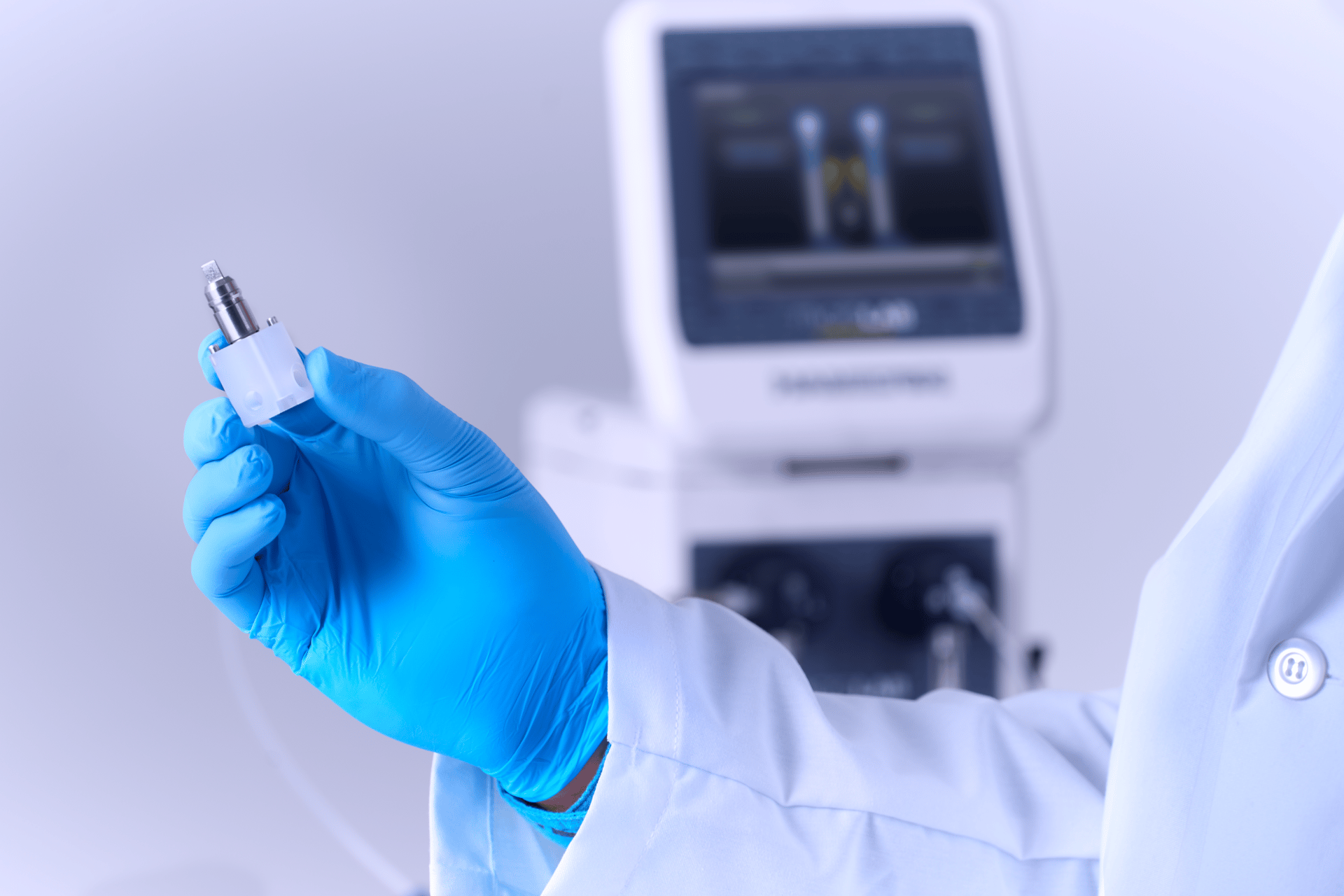 Gloved hand holding a sensor probe assembly in front of a blurred process analyzer with digital display