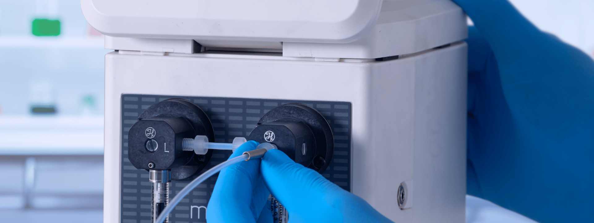 Gloved hands connecting tubing to a Hamilton MicroLab Controller syringe pump in a lab setting.