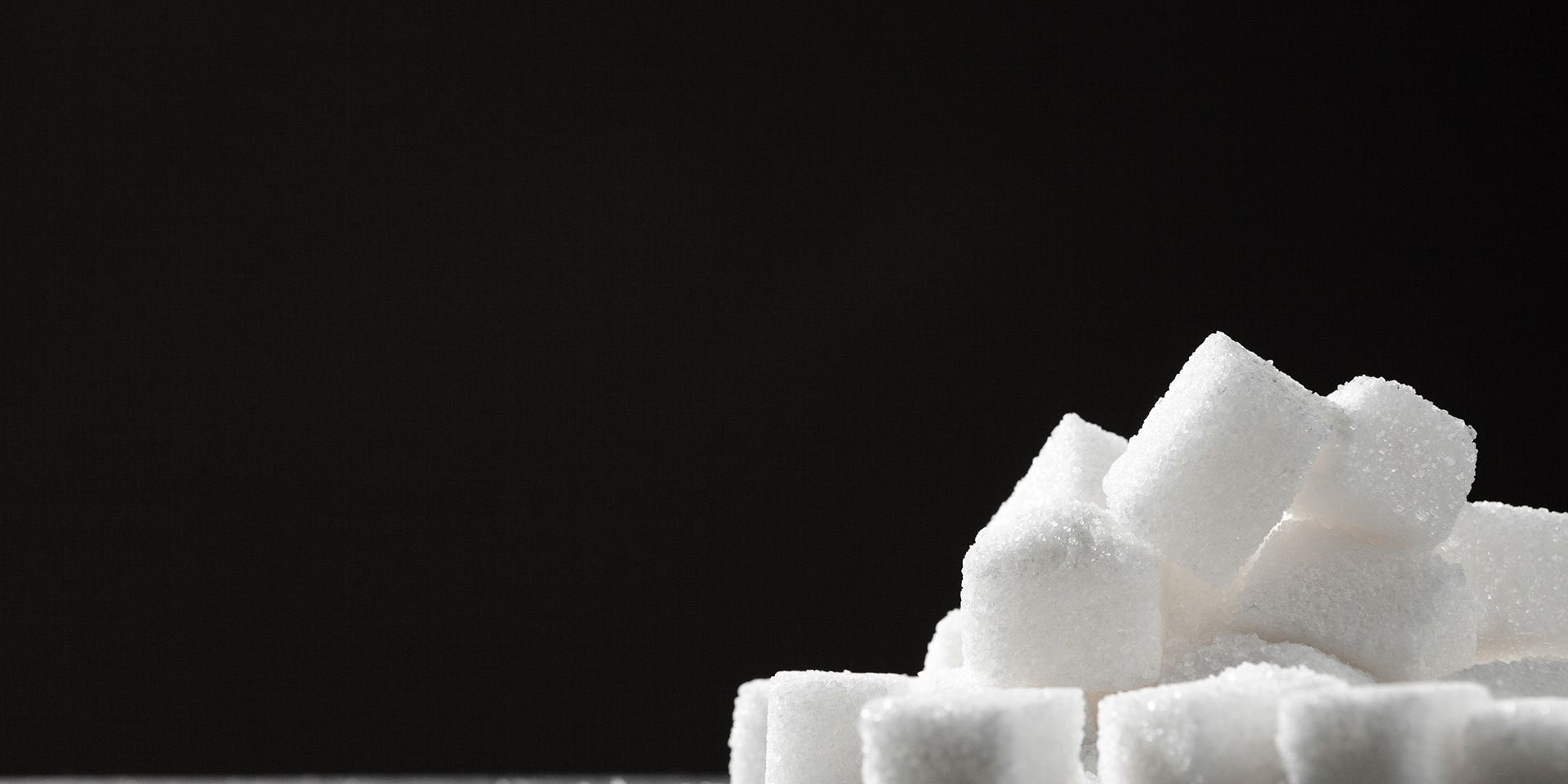 Pile of white sugar cubes with scattered granules on a dark surface