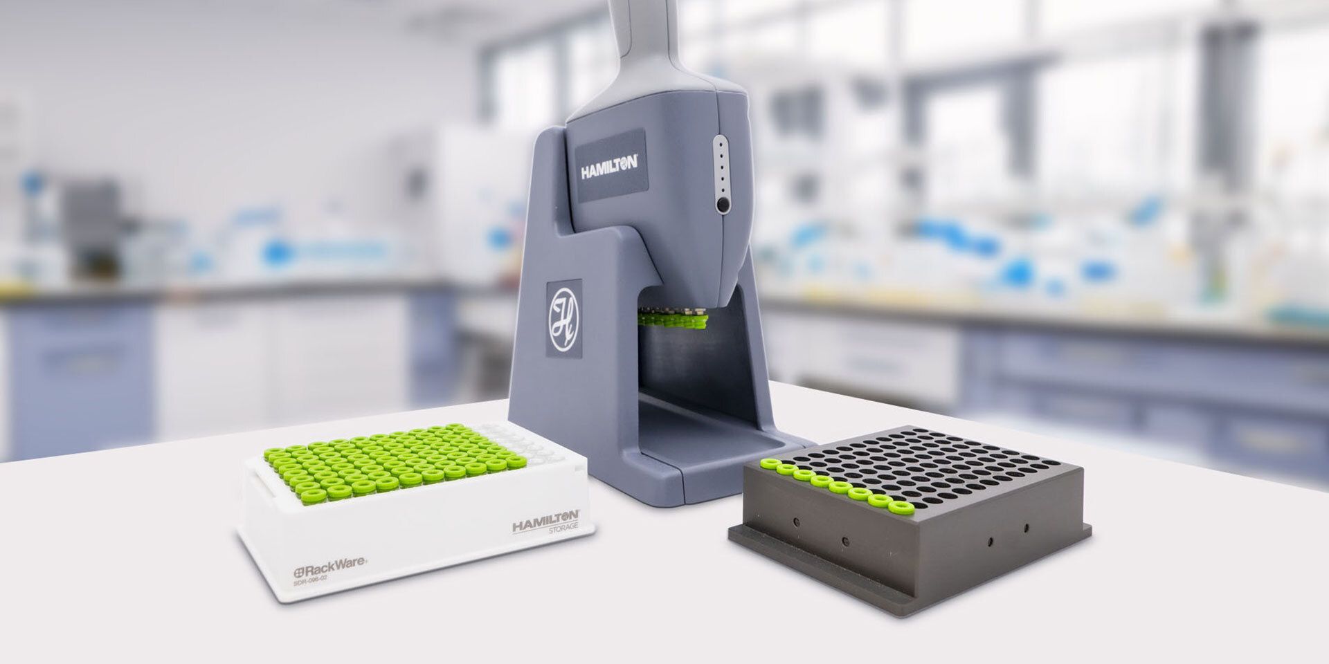 Hamilton handheld decapper with two sample tube racks holding green-capped tubes on a laboratory benchtop