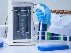 Gloved hand using a handheld pipette over a microplate beside a Hamilton MicroLab 600 Series dual-syringe dispenser