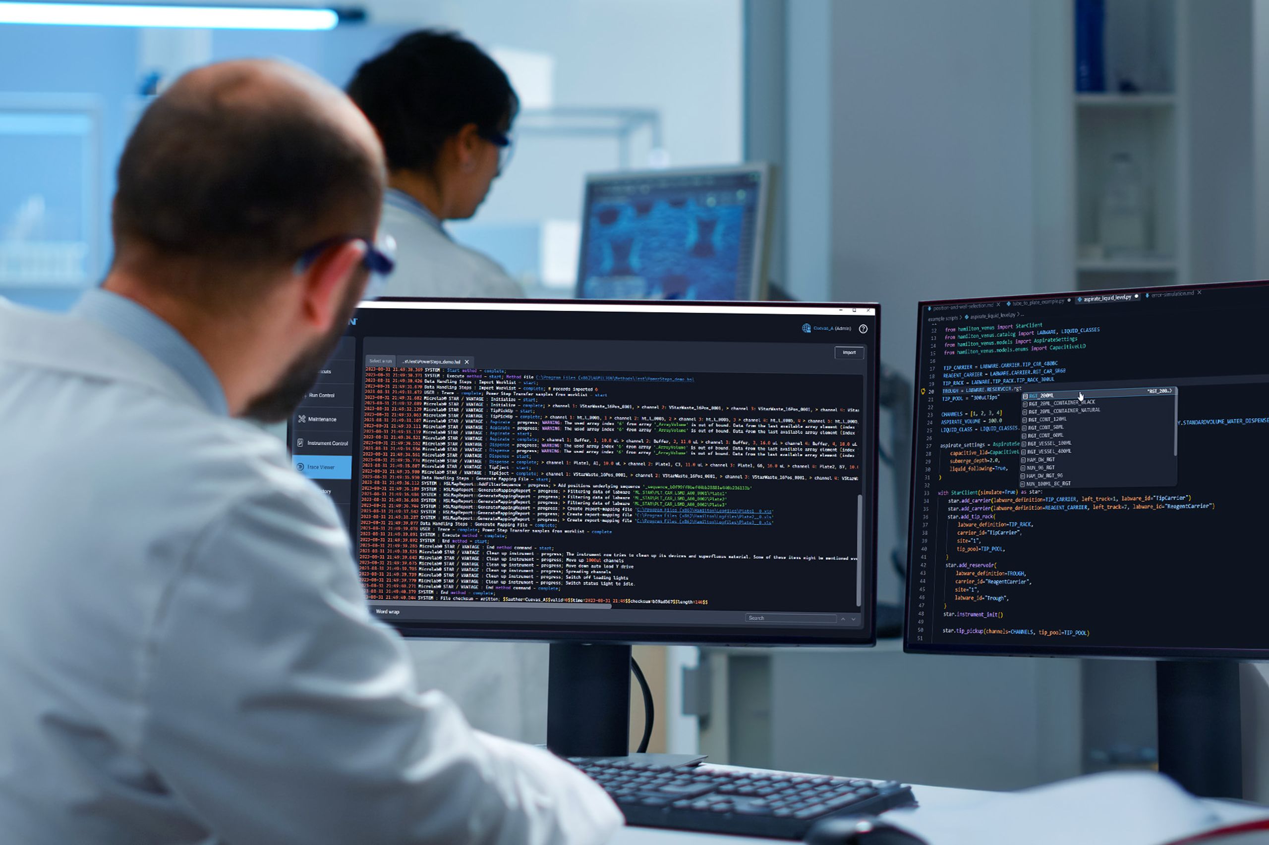 Person in a lab coat viewing dual monitors displaying Hamilton VENUS Python SDK code and system logs