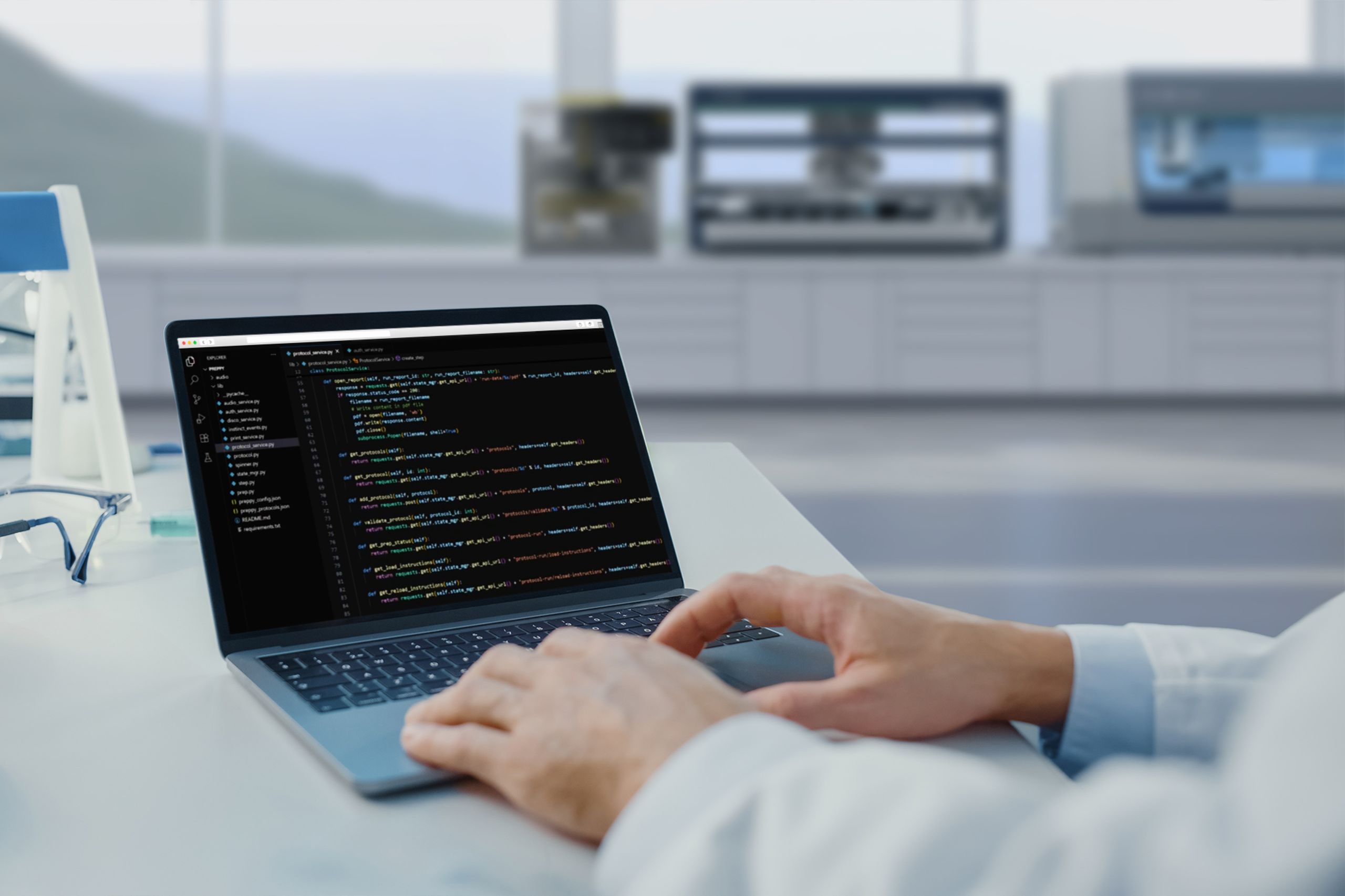 Hands typing on a laptop displaying Python code in a dark-themed IDE, in a lab setting