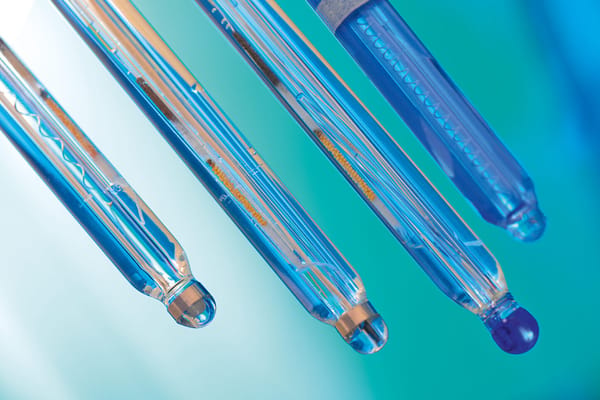 Close-up of four glass ORP sensor probes with blue electrolyte solution against a teal background