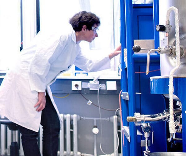 Lab technician in white coat and safety glasses adjusting blue bioprocessing equipment