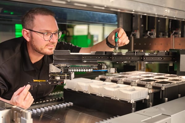 Engineer adjusting a robotic liquid handling system with a screwdriver inside an automated workstation