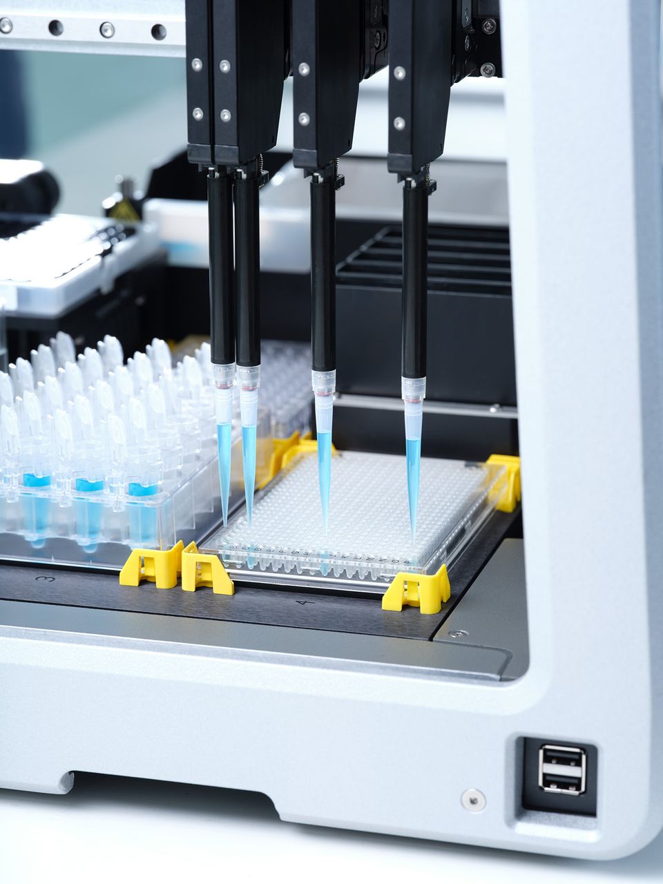 Automated liquid handler with four pipette channels and blue-tipped disposable tips dispensing into a microplate