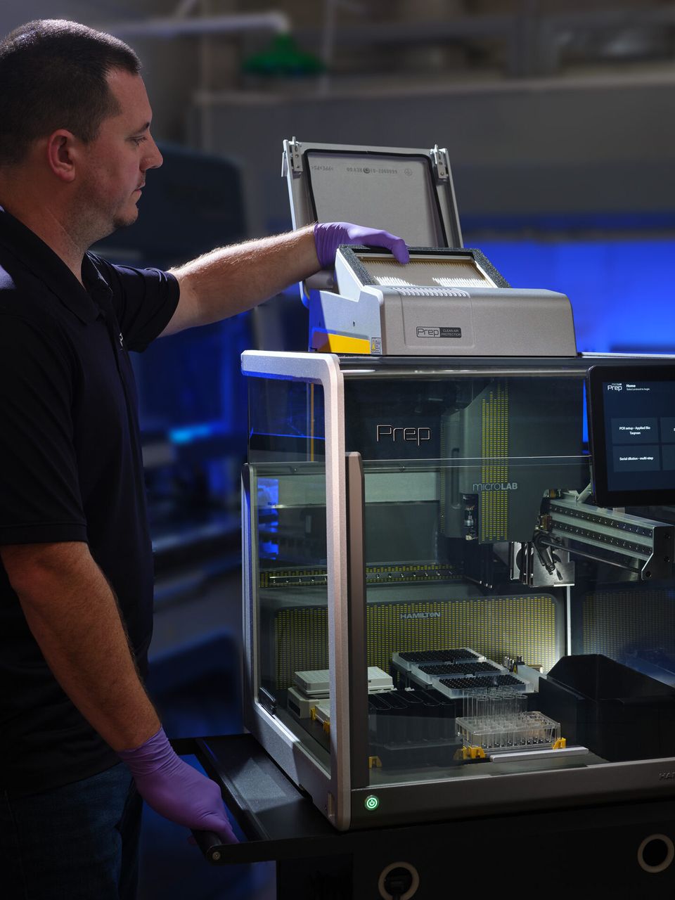 Lab technician in purple gloves loading a tray into a Hamilton MicroLab Prep automated liquid handler