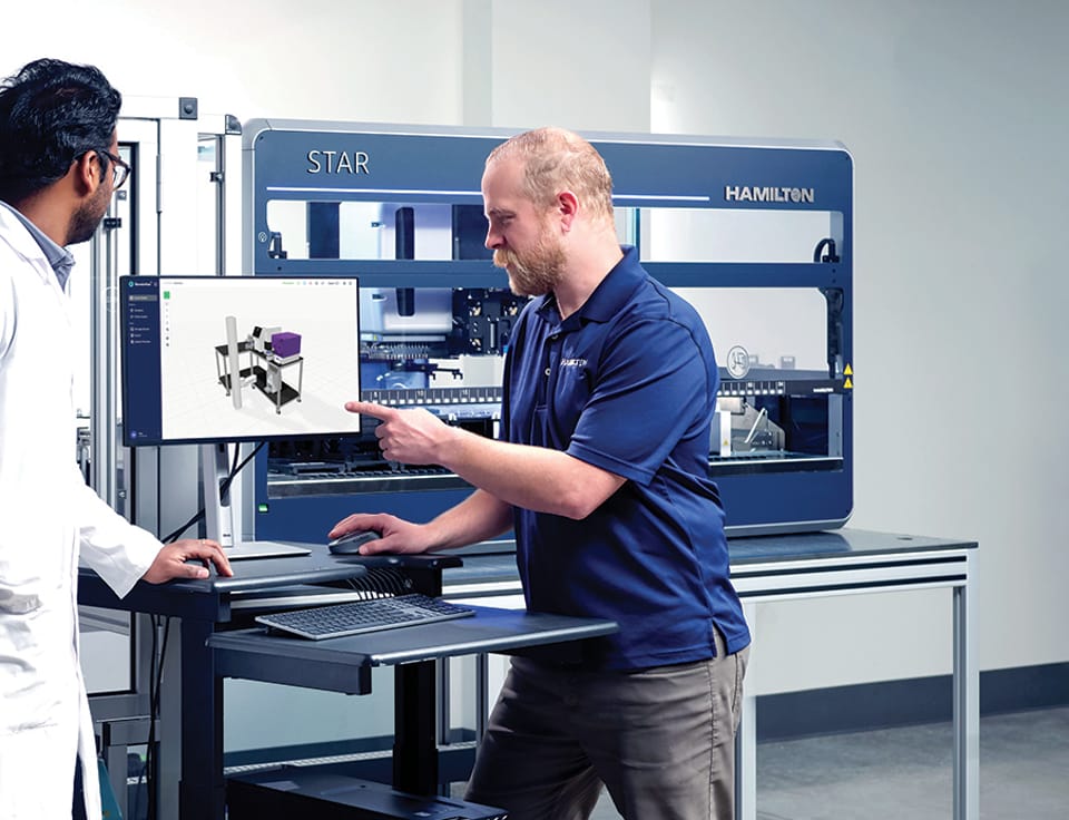 Hamilton STAR automated liquid handler with two lab personnel reviewing software on a monitor